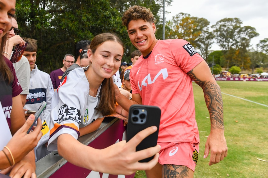 broncos player reece walsh poses for a selfie with a fan at a training event