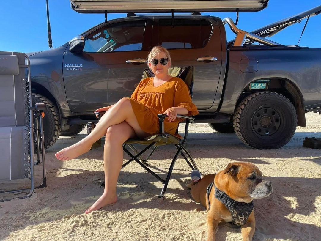 Tash sitting in a chair next to one of her dogs on the beach