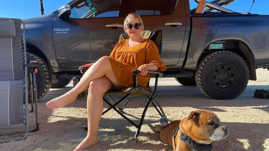Tash sitting in a chair next to one of her dogs on the beach