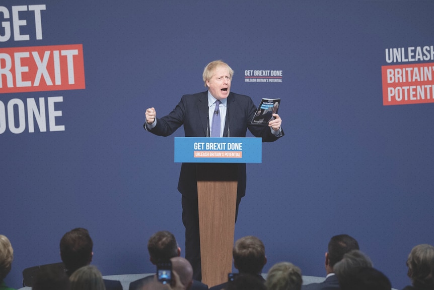 Boris Johnson stands behind a lectern on stage. The wall behind him reads: Get Brexit Done