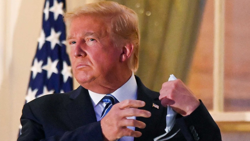 US President Donald Trump pulls off his protective face mask as he poses atop the Truman Balcony of the White House