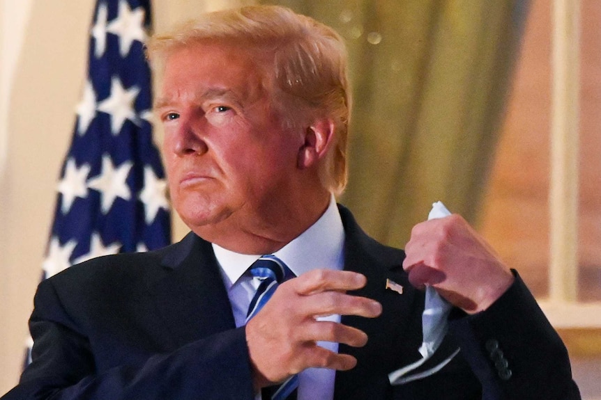 US President Donald Trump pulls off his protective face mask as he poses atop the Truman Balcony of the White House