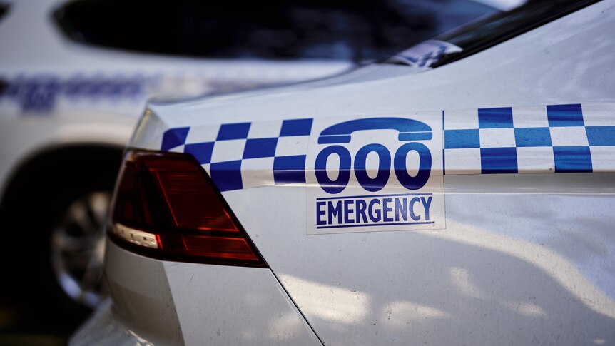 A close-up of the back of a police sedan with a focus on a '000 Emergency' sticker