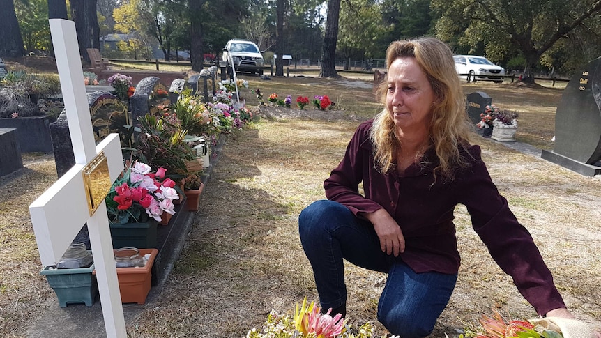 Debbie Wilson kneels beside her husband David's grave