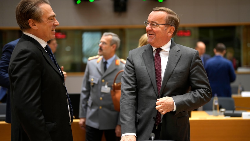 Two men are pictured wearing suits as they face each other.