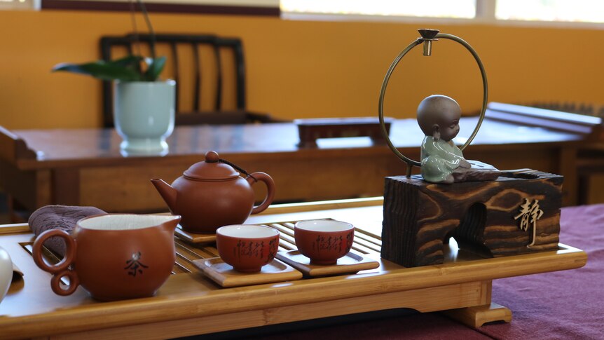 Close up of delicate brown and white chinese tea cups and teapot with a small statue. 
