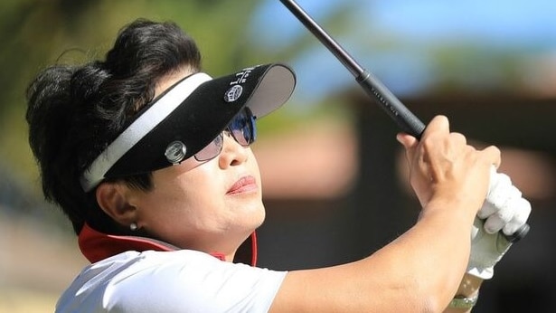 An asian woman swings a golf club, wearing a polo shirt, a visor and a glove.