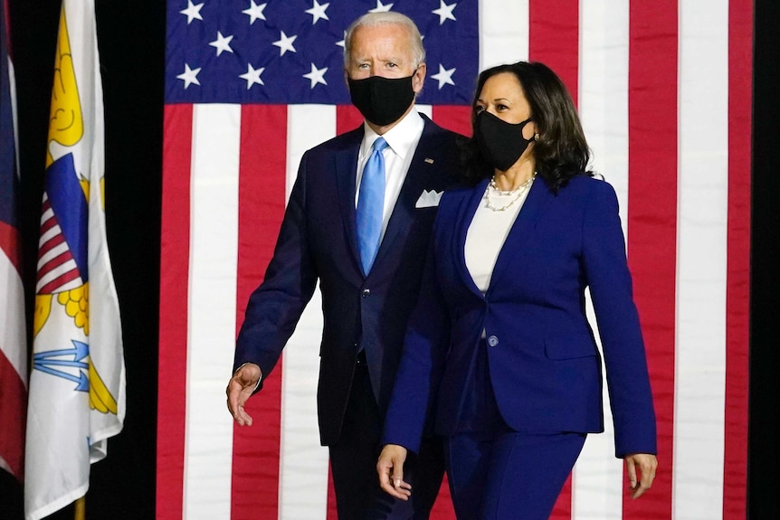 Joe Biden and Kamala Harris walk in front of a US flag.