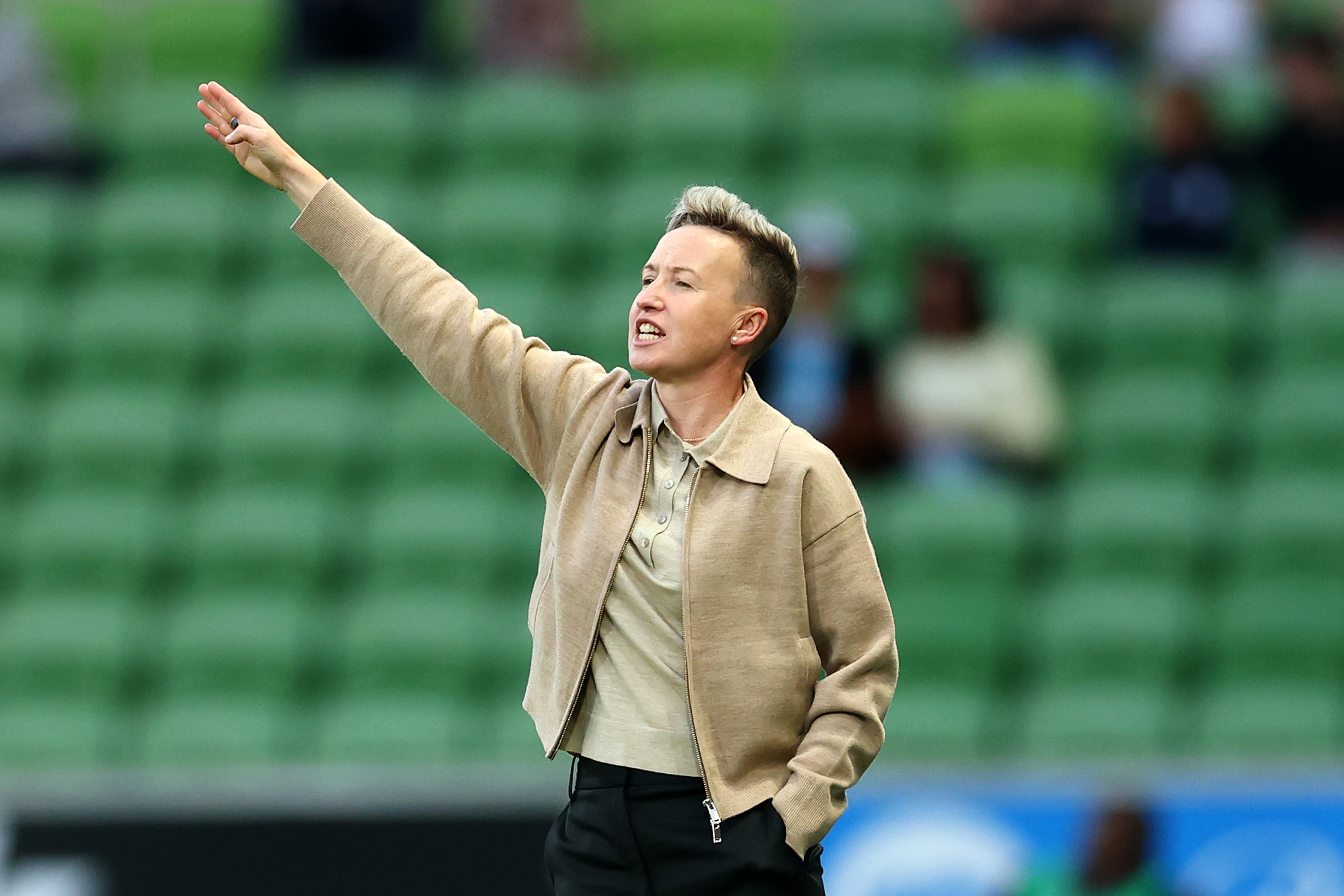 An A-League women's coach holds her arm out to the right to direct players during a grand final.