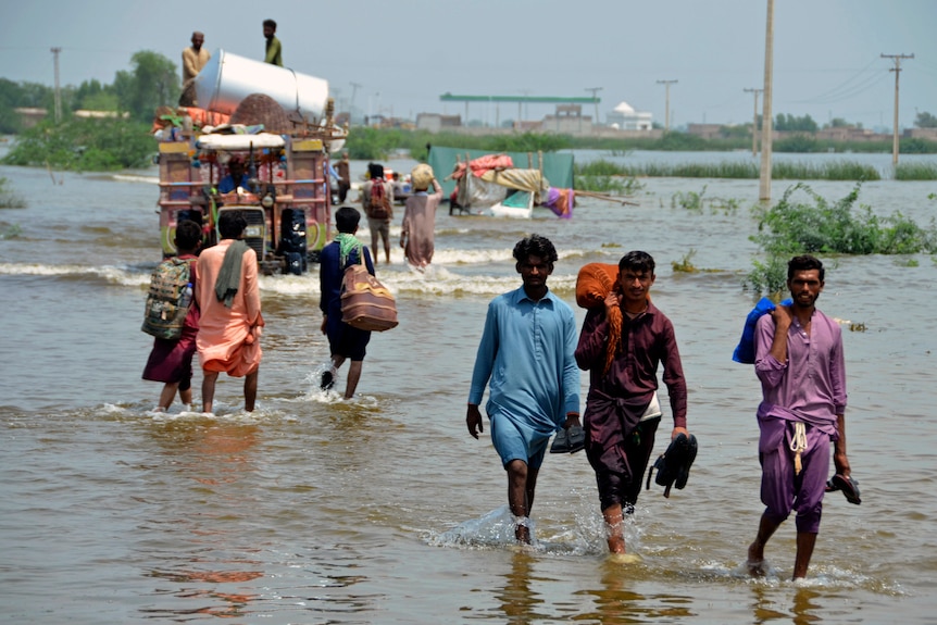 Des gens pataugent dans les eaux de crue avec leurs affaires au Pakistan. 