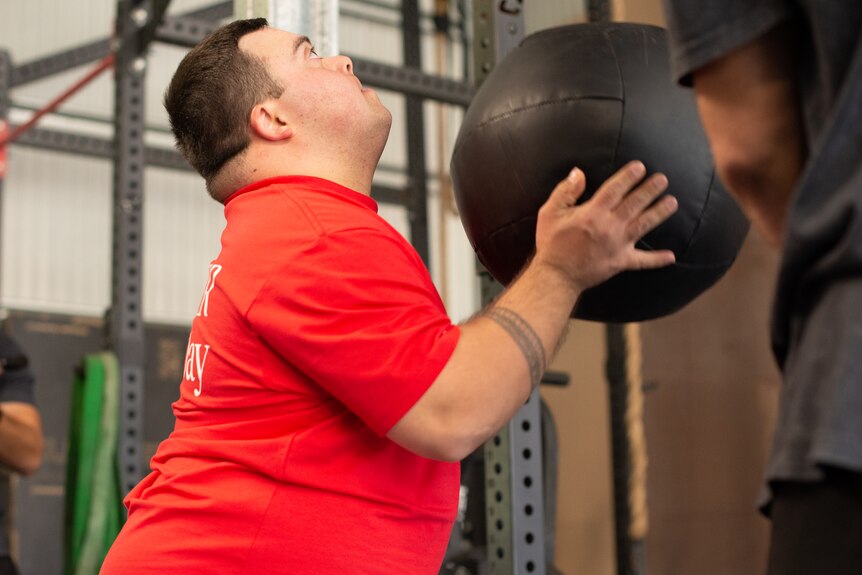A young man holds a large weighted exercise ball.
