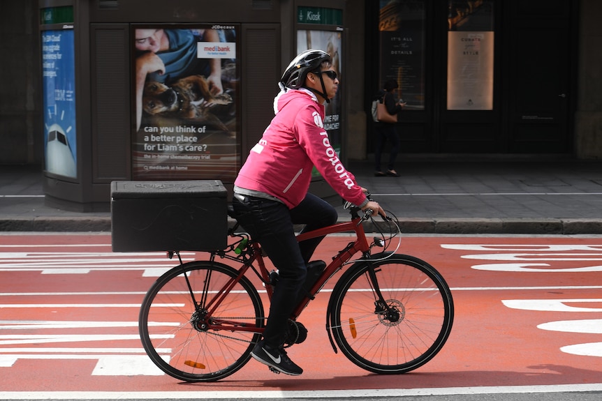 A food delivery rider on a bike on a street. He is wearing a pullover with "foodora" printed down his sleeve. 