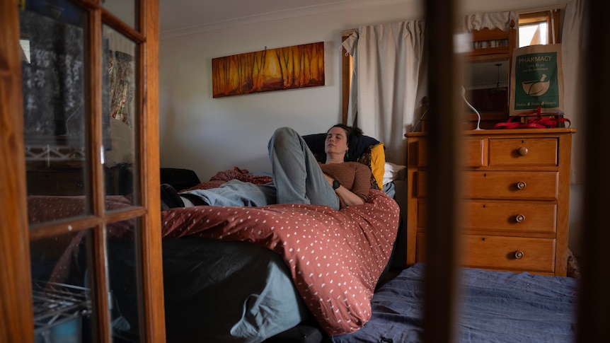 A lady lays down in bed with her eyes closed.