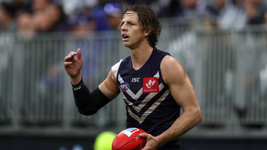 Nat Fyfe raises his hand while holding the ball.