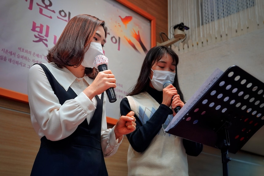 Two Korean women in face masks singing 