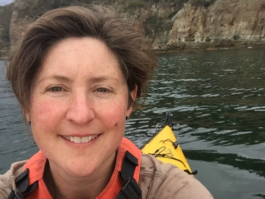 A woman wearing an orange and yellow life jacket smiles at the camera from a yellow kayak