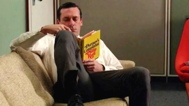 Don Draper from the TV show Mad Men reads a copy of Portnoy's Complaint.