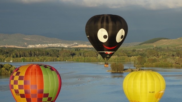 A black balloon with a smiley face next to other balloons.