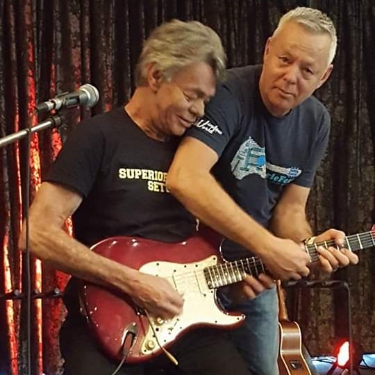 Two men play one guitar on stage.