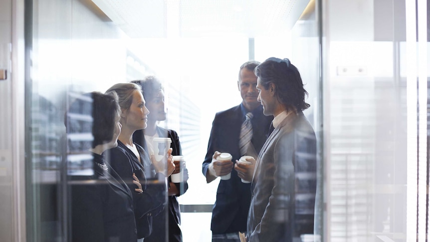 Business people stand in an lift together, holding takeaway coffee cups.