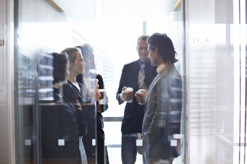 Business people stand in an lift together, holding takeaway coffee cups.