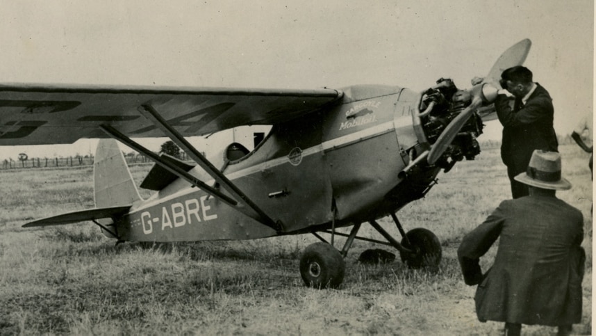 Black and white image of monoplane, and man fixing the front of the aircraft. 
