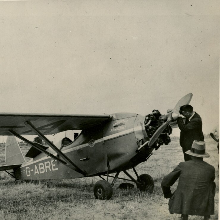 Black and white image of monoplane, and man fixing the front of the aircraft. 