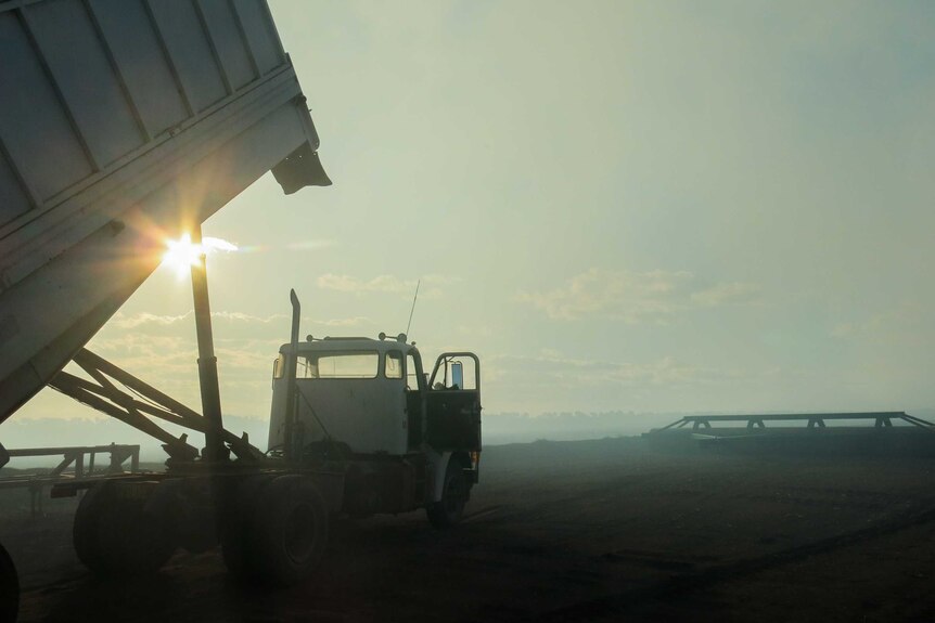 The sun peeks behind a truck as it unloads fertiliser, standing in a smoky paddock.