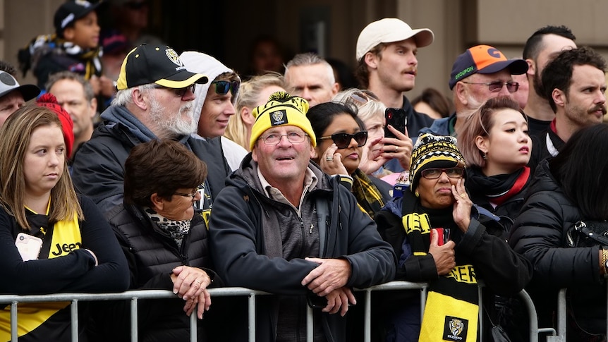 A group of AFL fans wearing Richmond Tigers merchandise look on as the grand final parade takes place.