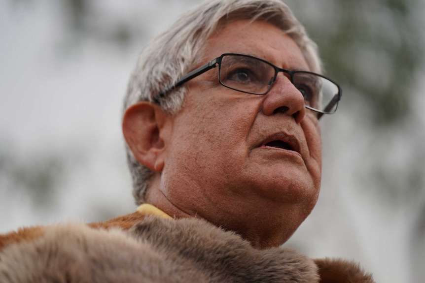 An Aboriginal man with glasses wears a ceremonial gown.