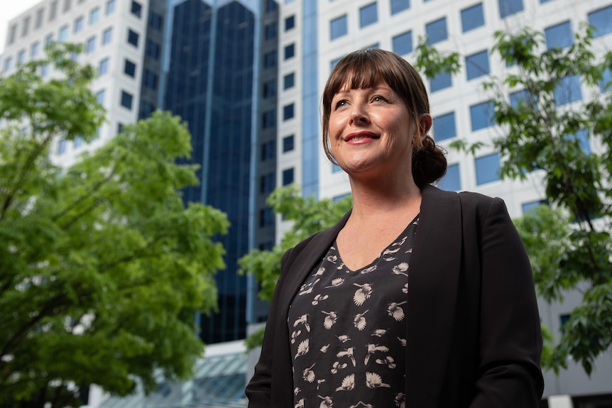 A woman stands in front of a large office building.