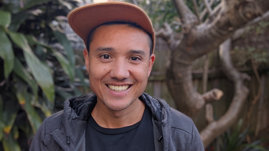 Seiji Armstrong wears a cap with leaves and branches in background. 