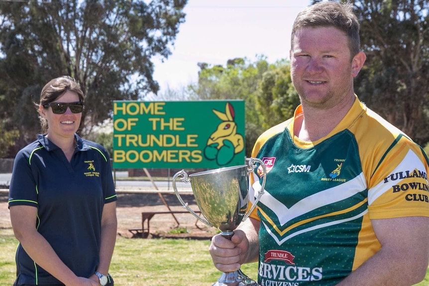 A woman and man who is holding a silver cup standing on an oval in front of a sign saying Home of the Trundle Boomers