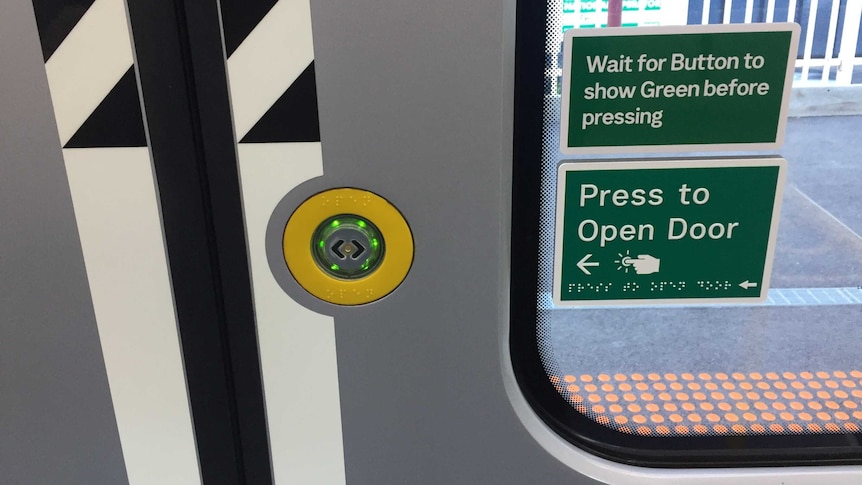 train door with green lit button ringed with yellow and sign reading "Wait for Button to show Green before pressing