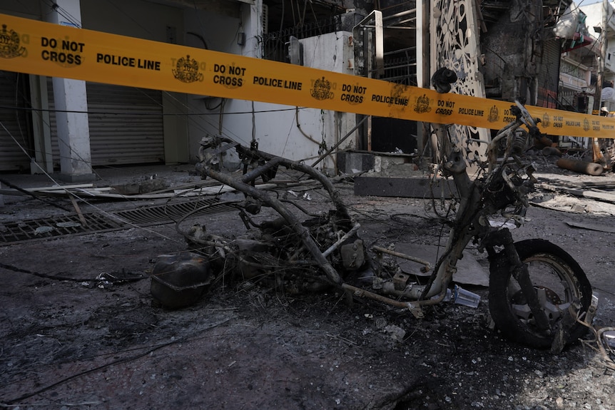 A burned out small bicycle among rubble with yellow police tape in front.