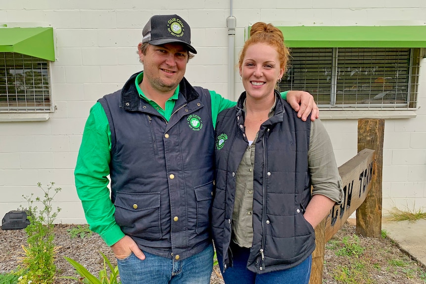 A man and a woman in farming gear stand smiling on a property.