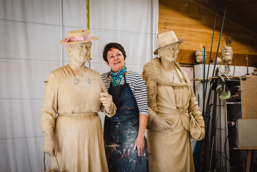 A woman standing between two statues. 