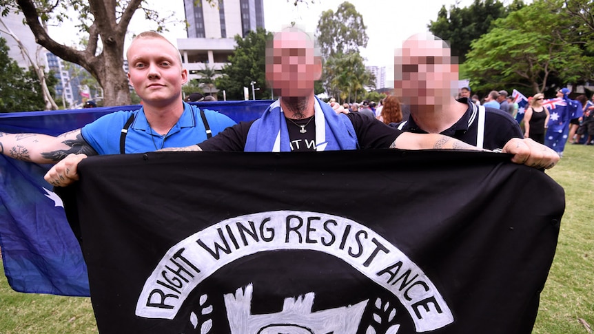 Three men standing behind flag.
