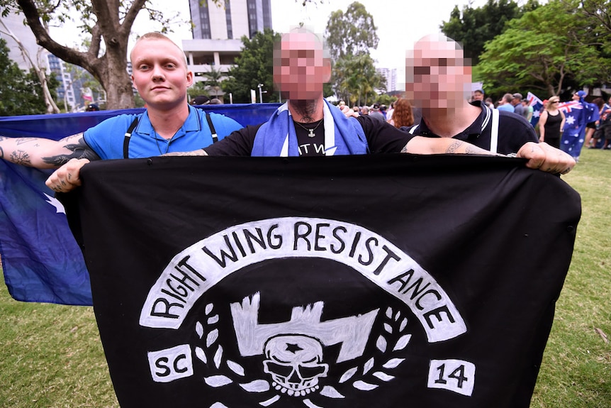 Three men standing behind flag.