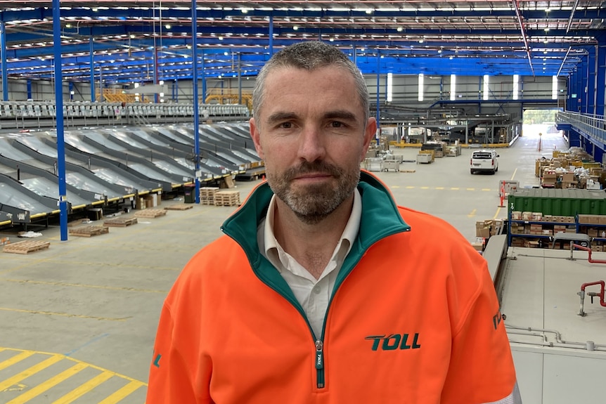 A man in an orange and green jumper looks at the camera in a big warehouse