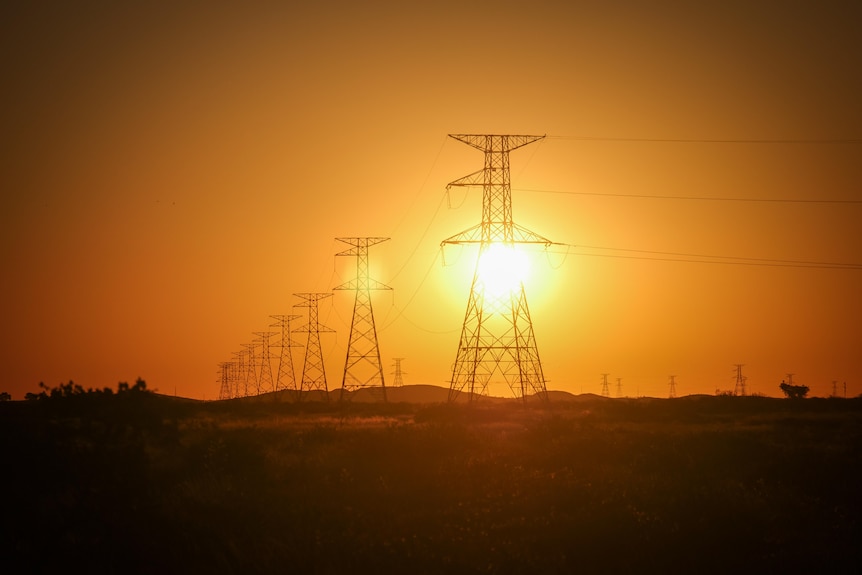 Silhouette of transmission lines at dusk with sun flaring through