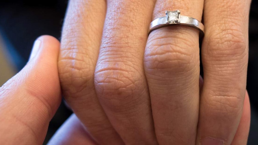 Man holds woman's hand who is wearing an engagement ring.