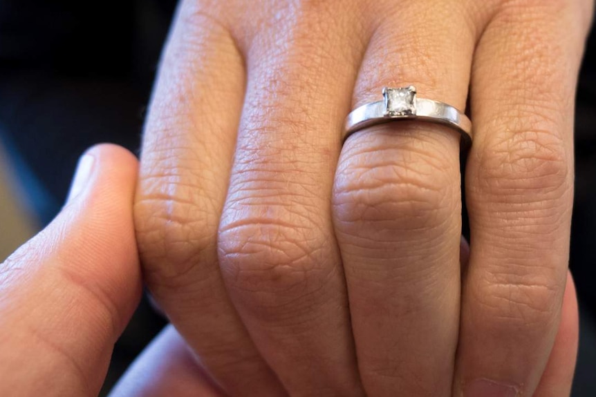 Man holds woman's hand who is wearing an engagement ring.