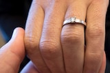 Man holds woman's hand who is wearing an engagement ring.
