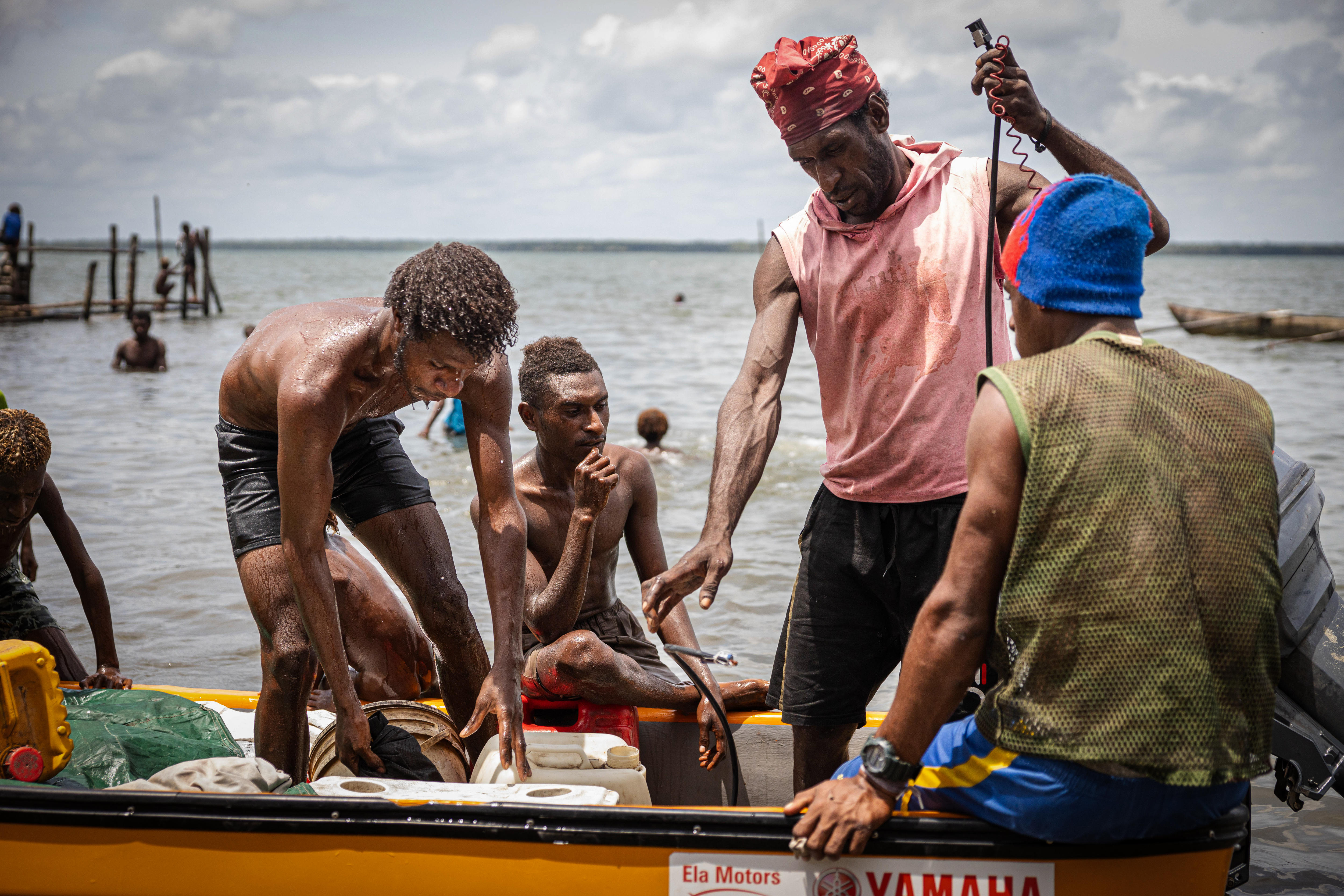 Men stand on a boat preparing to lift heavy bags out and onto the sand