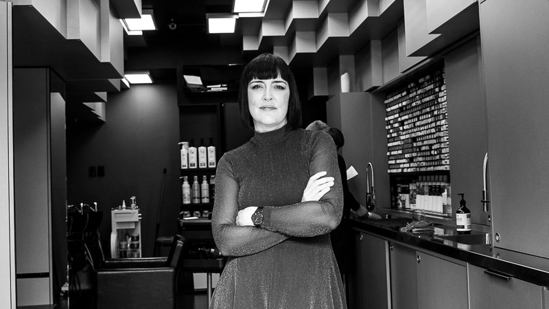 Black and white image of a women with her arms folded in a hair salon