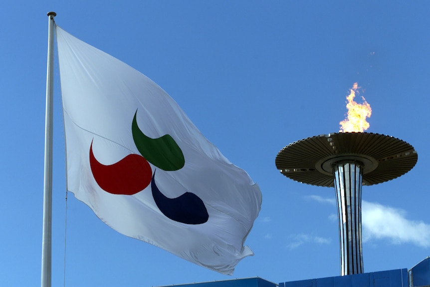 The Paralympic flag featuring the three agitos in blue, green and red stands next to a metal cauldron with fire coming from it