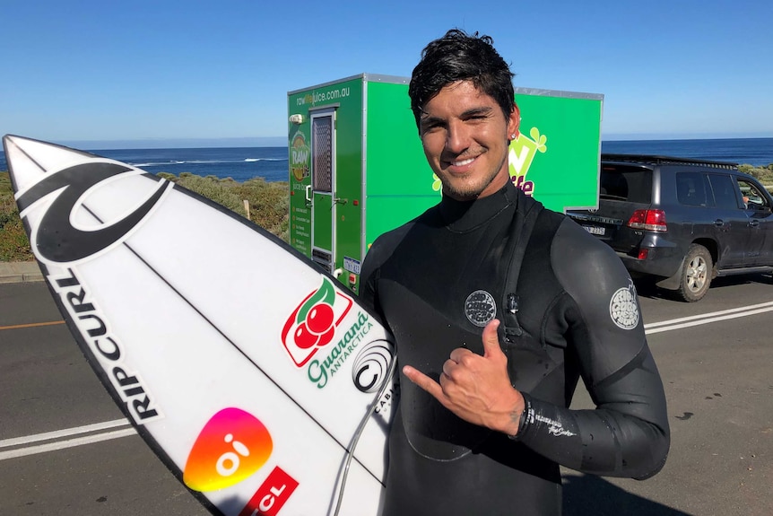 A Brazilian surfer in a wetsuit with a board under his arm