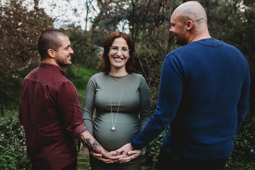 A pregnant woman with a man standing on either side of her