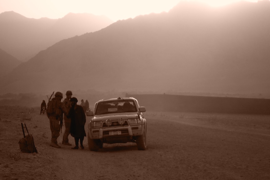 A car on a dusty road with soldiers 